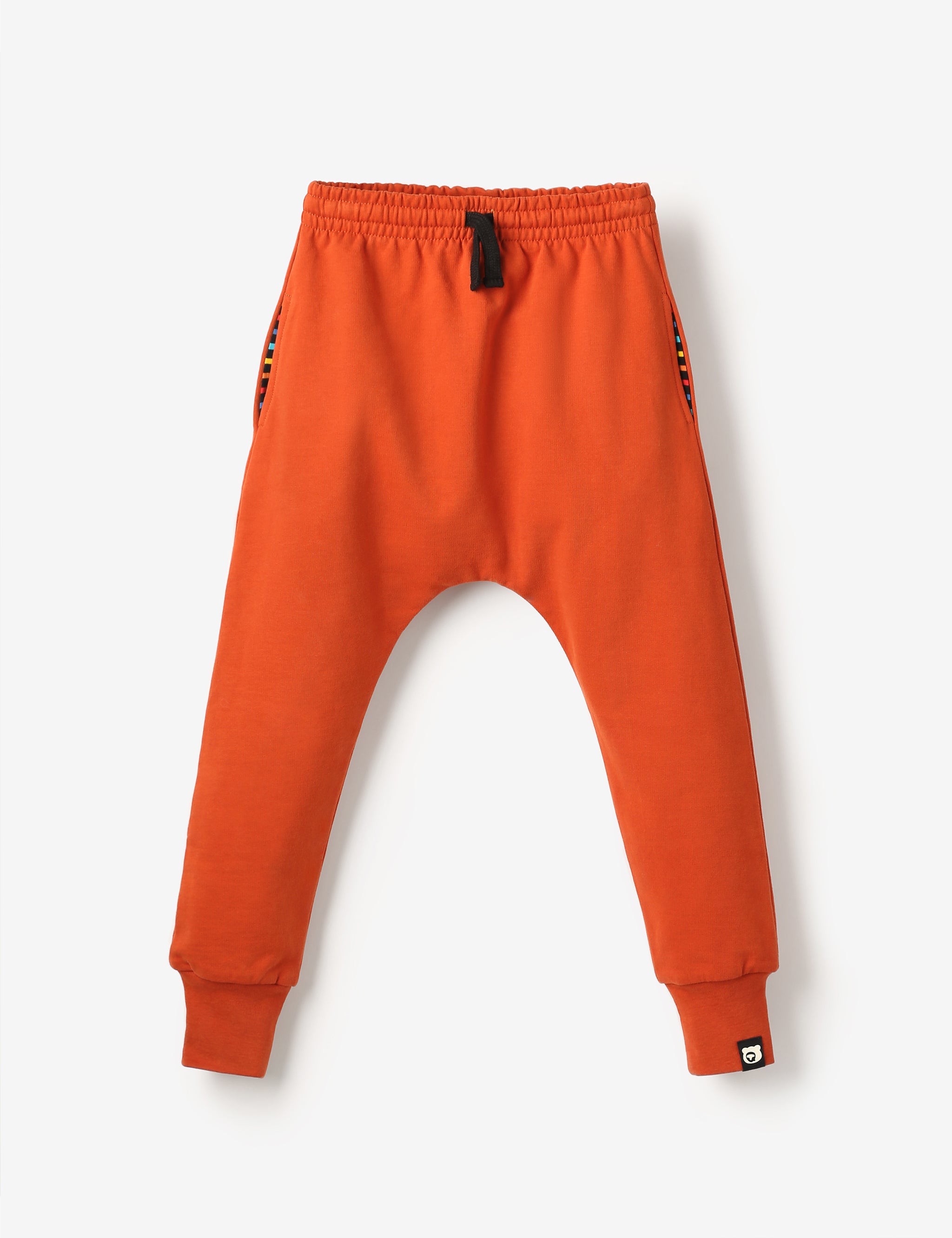 Flat lay of red brick coloured kids joggers with, made from soft GOTS-certified organic cotton terry – unisex, sensory-friendly, comfy and perfect for any adventure.